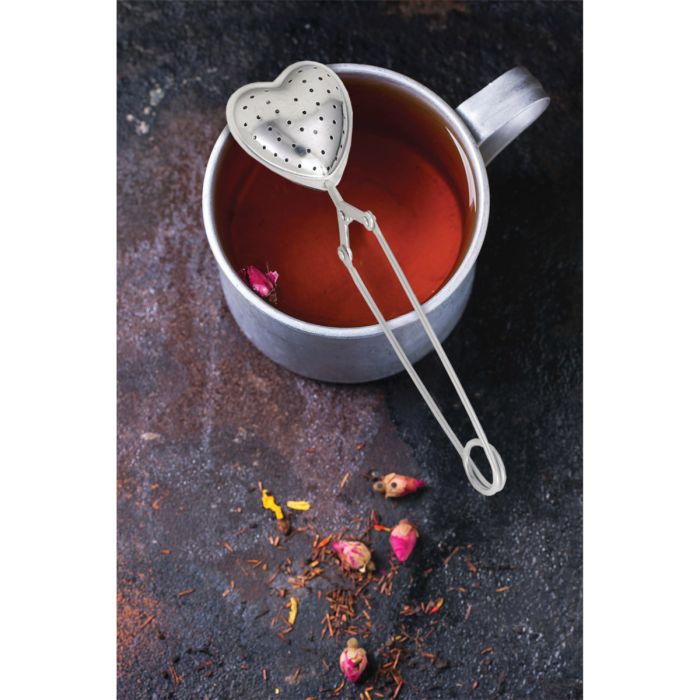 Heart shaped stainless steel tea infuser with a cup of tea on a dark background 