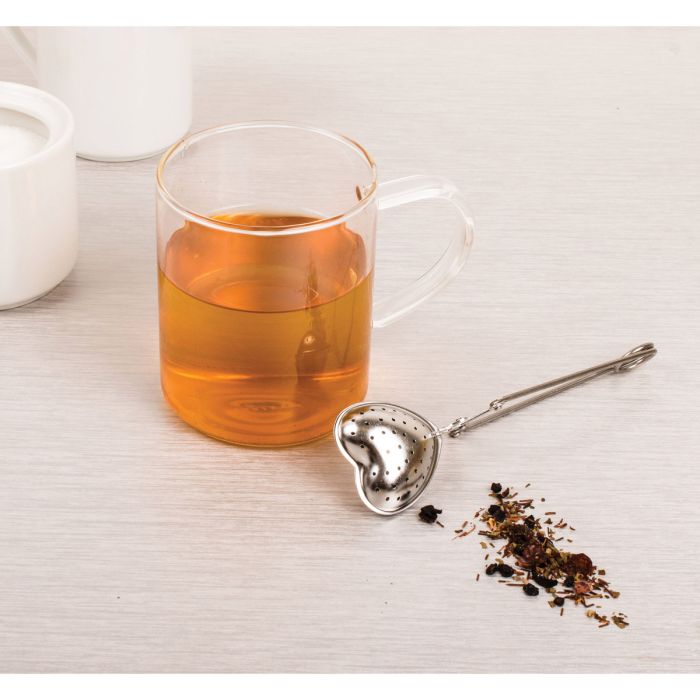 Heart shaped stainless steel tea infuser with a cup of tea on a neutral background 